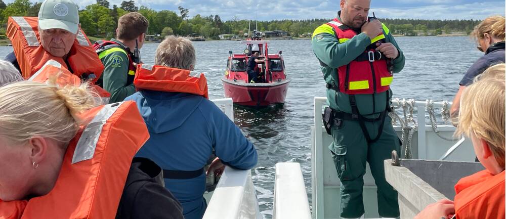 Flera personer iklädda flytväst syns i bild ombord på en båt. På båten finns också två män iklädda ambulansuniformer. En röd räddningstjänsbåt närmar sig.