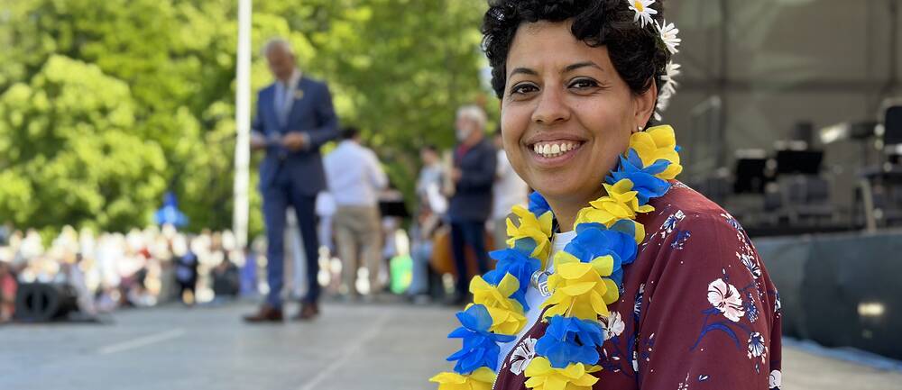 Porträttbild på en leende kvinna med blomkrans i håret och girlanger runt halsen med svenska flaggans färger på väg upp på scen.