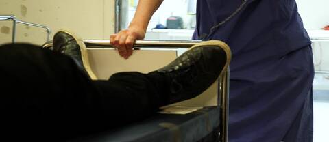 Närbild på ben på en patient som skjutsas i en sjukhussäng av personal i ett sjukhus.