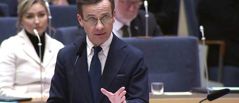 Ulf Kristersson i talarstolen i Sveriges riksdag med Ebba Busch (KD) och Johan Pehrson (L) i bakgrunden.