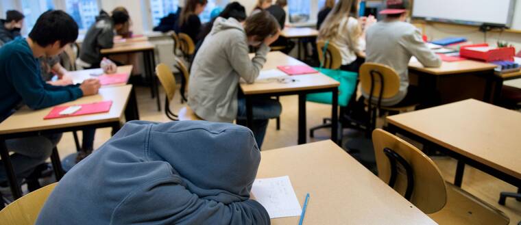 En trött högstadieelev i årskurs 8 sover med huvudet på bänken under en lektion