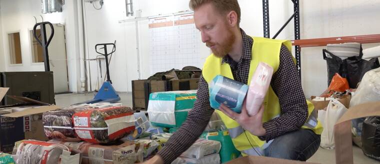 en man i skjorta och varselväst plockar paket med blöjor i en lagerlokal