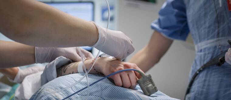 Person som ligger i sjukhussäng med monitor bakom. Man ser bara personens arm. Sjukvårdspersonal står bredvid och fäster slangar vid personens hand. Sverige har 21 regioner. De styr över sjukvården. Tidigare var det landstinget som hade hand om vården.
