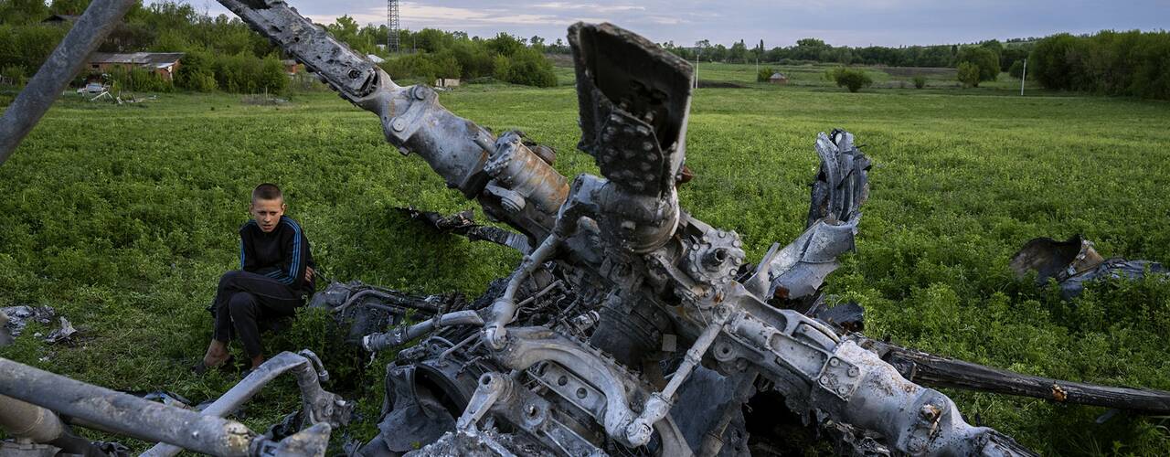 En pojke sitter bredvid skrotet efter en förstörd rysk helikopter i Malaya Rohan i Charkivregionen i Ukraina.