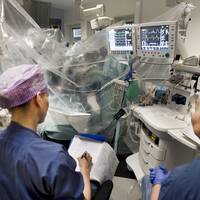 Vårdpersonal i operationskläder sitter bredvid en pågående operation i en sjukvårdssäng.