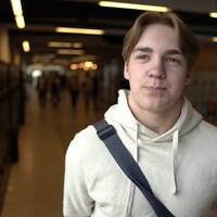 En elev bärandes axelremsväska och ljus huvtröja intervjuas i korridoren på en gymnasieskola i Umeå