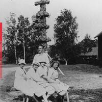 En svartvit bild från cirka 1920 – 1940. Fyra kvinnor och en man står framför midsommarstången i Mora by i Eskilstuna kommun.