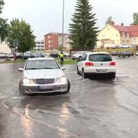 Två bilar kör längs en vattenfylld gata.