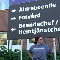 kvinna står under stor skylt med pilar till äldreboende, fotvård och boendechef/hemtjänstchef