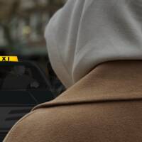 Anonym kvinna står med ryggen mot kameran iklädd huvtröja, framför en illustration av en taxibil.