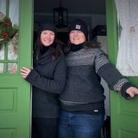 Bild på Jenny och Jenny som har på sig tjocka tröjor och mössa när de står i dörröppningen till sitt hus i Åbyggeby, där de lyckats minska elförbrukningen rejält.