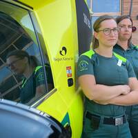 Två kvinnliga ambulanssjuksköterskor står med korsade armar framför en ambulans.