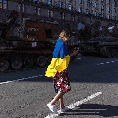 En kvinna med en ukrainsk flagga går förbi ryska militärfordon i Kiev. Bild från augusti 2022.