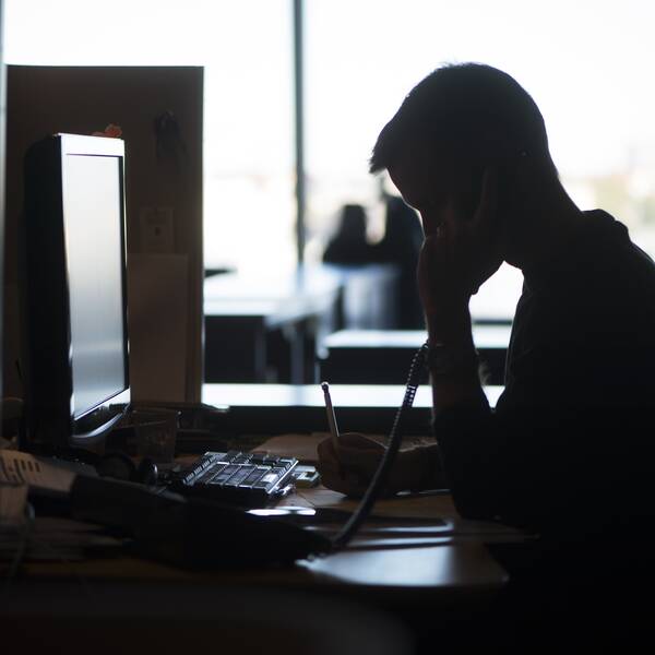 Anonym man i profil som sitter vid ett skrivbord och talar i telefon.