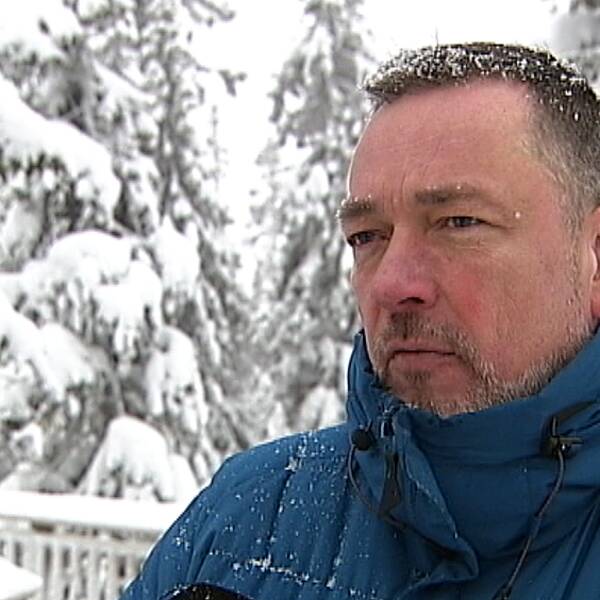 en man i dunjacka framför snöig skog