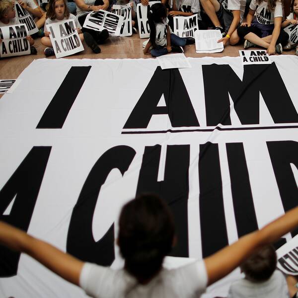 Barn sitter med plakat och en banderoll där det står ”Jag är ett barn”
