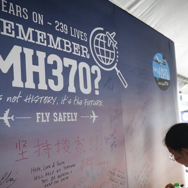 En ung tjej skriver ett kondoleansbudskap på en affisch som påminner om årsdagen av dagen då planet MH370 försvann.