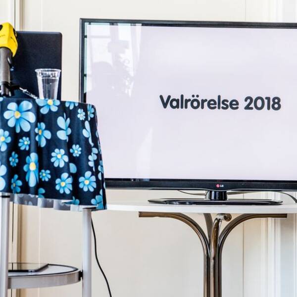 mikrofoner står på bord med SD-logotyp på duken, en bildskärm med texten ”valrörelse 2018”)