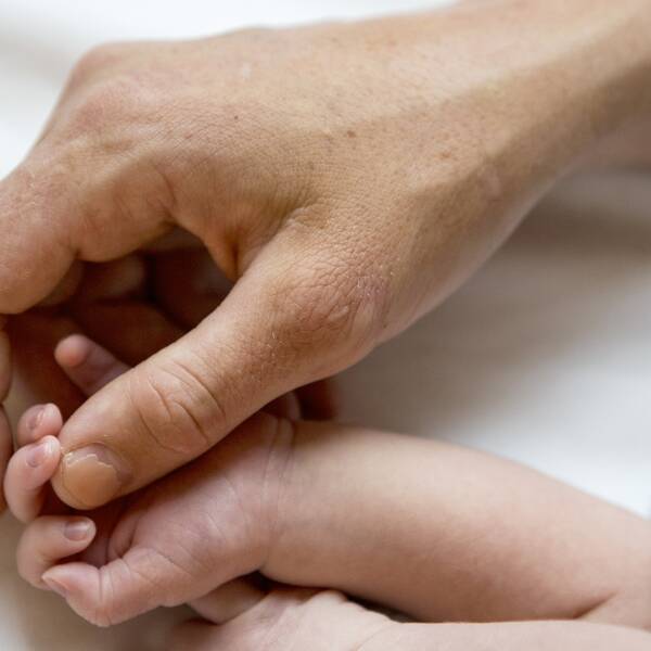 En bild på en hand som håller om ett nyfött barns hand.