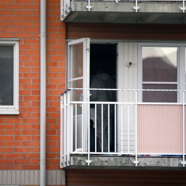 Husfasad med balkong med öppen dörr. Polistekniker skymatar i lägenheten