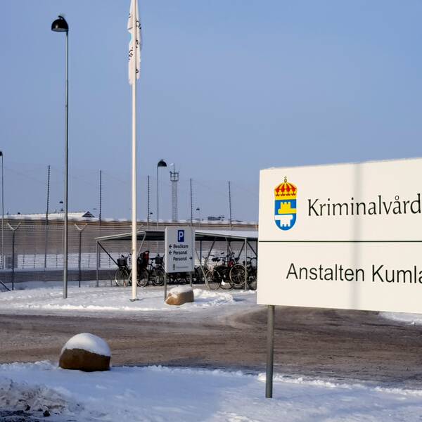 En skylt med orden Kriminalvården och Anstalten Kumla. Skylten står vid parkeringen utanför Kumlaanstalten, till vilken man ser stängslet i bakgrunden.