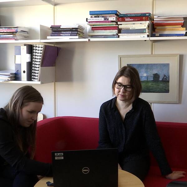 En bild på reportern som visar ett reportage för en forskare. De sitter på ett kontor med en röd soffa.