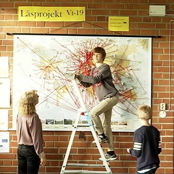 Karta med röda streck. Elever på Stallarholmsskolan i Strängnäs. Pojke klättrar upp för stege. Lärare tittar på elev och karta.