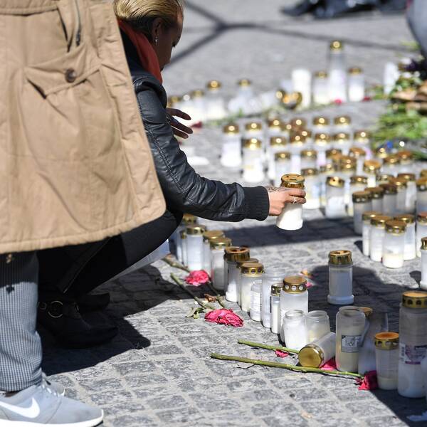 En person tänder ljus vid en minnesplats för de tre personer som dödats i skjutningar i Sätra i Stockholm. 