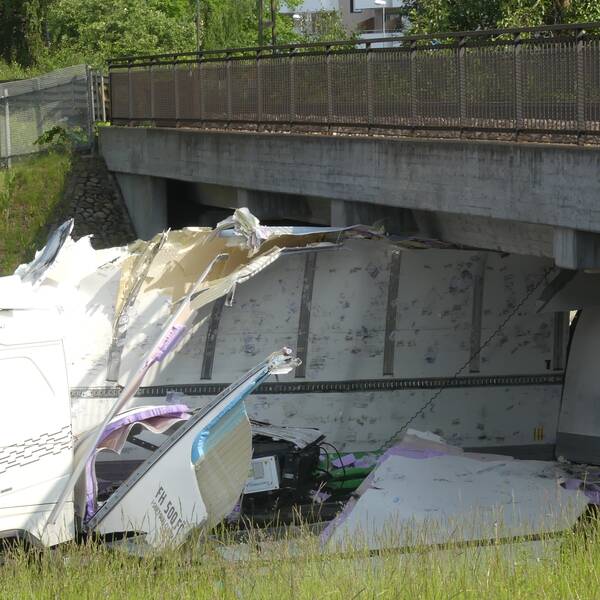 En lastbil sitter fast mitt under järnvägsbron. Sidorna på lastbilen har slagits sönder och ligger utfläkta över asfalten.