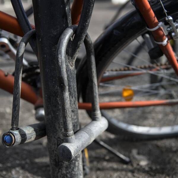 En cykel står parkerad i ett smutsigt cykelställ. Två cykellås hänger från cykelstället.