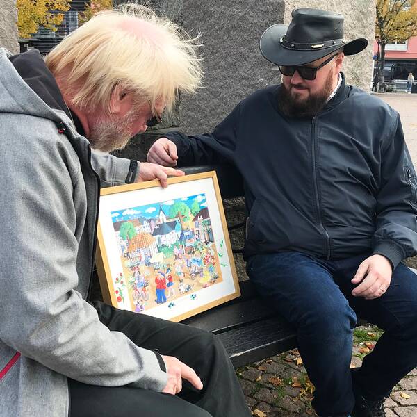 Initiativtagaren Fredrik Jansson och tidigare ordföranden Ewe Windahl tittar på ett konstverk av Rosfestivalen, målat av en lokal konstnär.