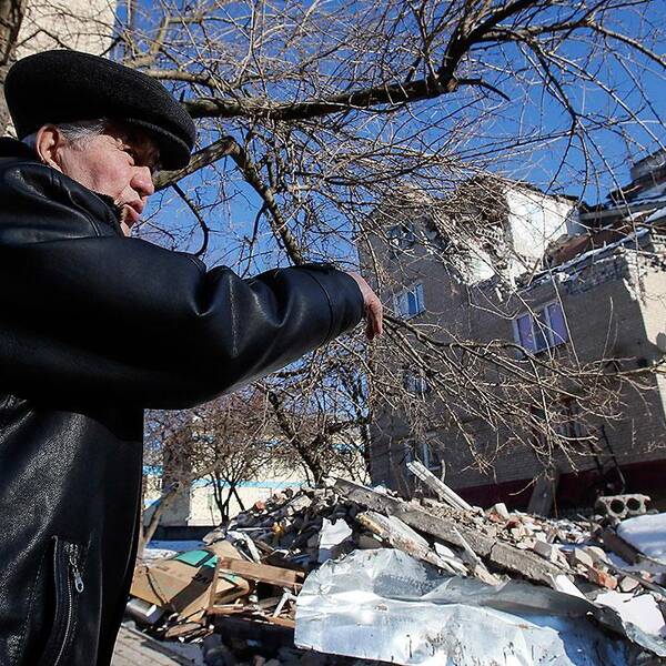 En man i staden Dokuchayevsk pekar på ett hus som träffats av granateld.