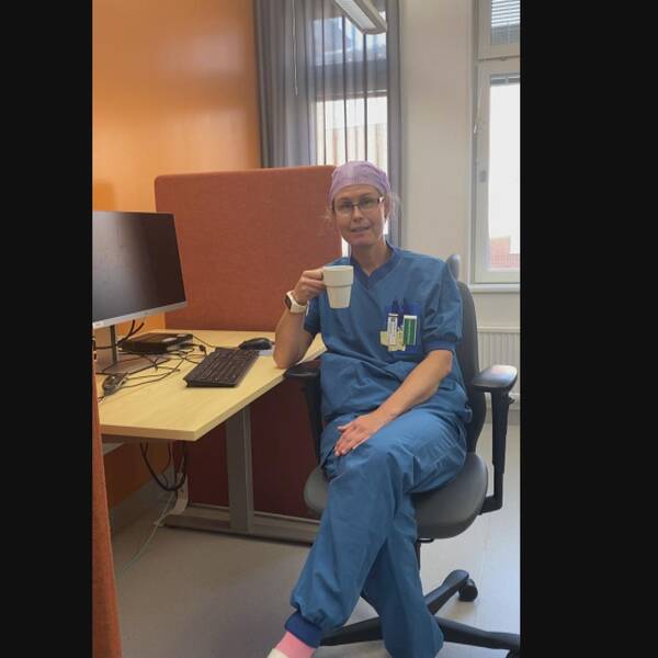 Therése sitter i arbetskläder i ett datarum på sjukhuset med en kaffekopp i handen och ler snett.