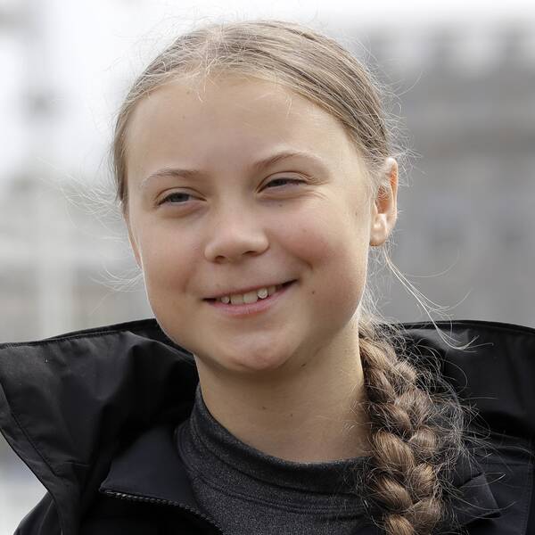 Greta Thunberg i svart jacka och fläta, ler mot kameran.
