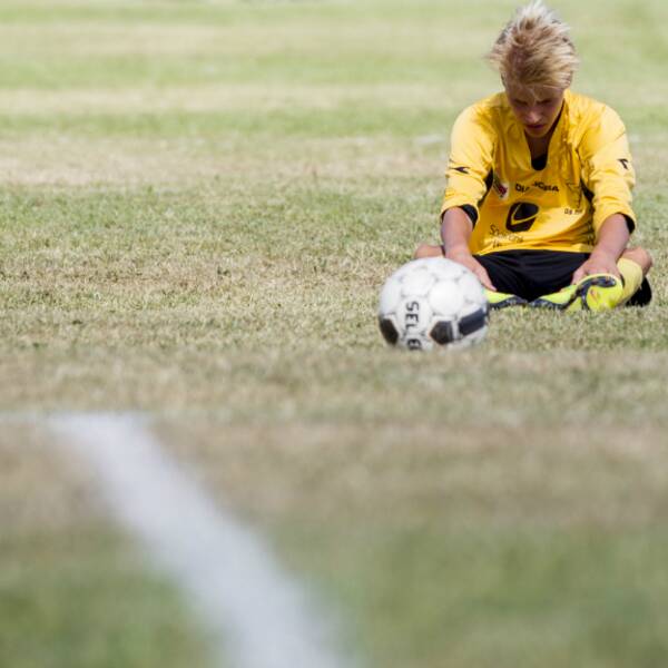 En ung ensam fotbollsspelare sitter på gräsmattan och deppar