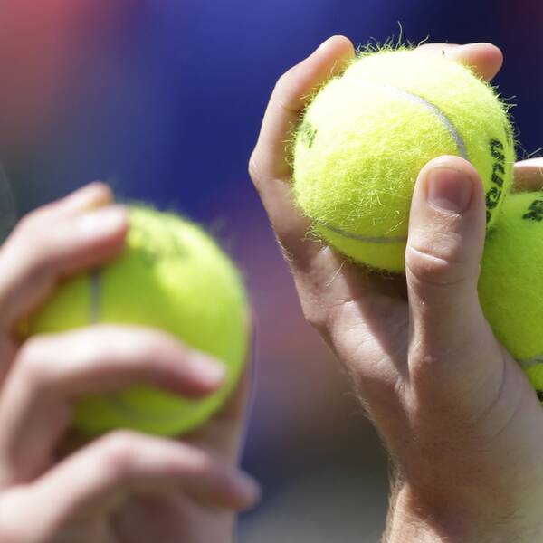 Två händer som  båda håller i tennisbollar.