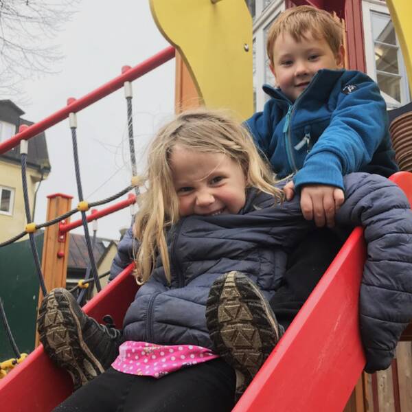 två barn i femårsåldern sitter i en rutschkana.