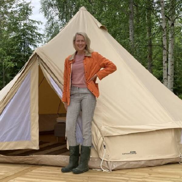 en kvinna står framför ett tält på ett trädäck med skog i bakgrunden