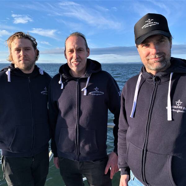 Tre män med blått hav i bakgrunden.