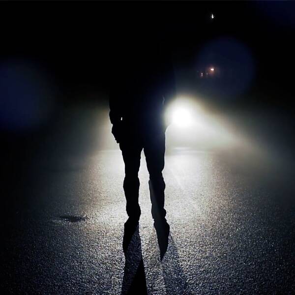 En person står framför strålkastare på en väg.