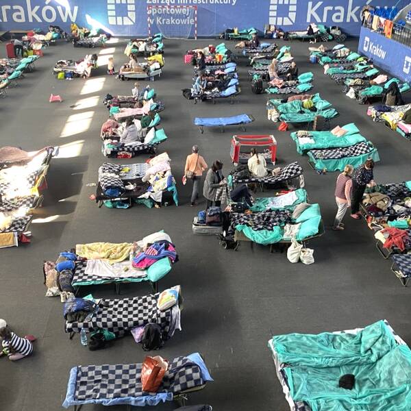 Ukrainska flyktingar samlade i en sporthall, i hallen står tältsängar rad på rad med flyktingarnas saker runt.