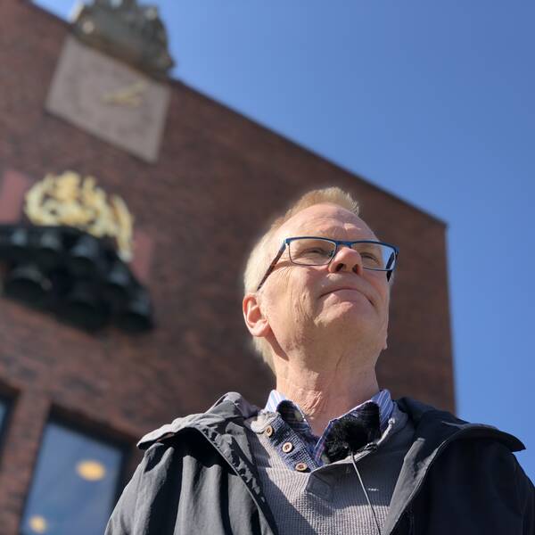 Jörgen Johansson står framför rådhuset i Halmstad. Bilden är tagen underifrån så att både han och klockspelet syns.