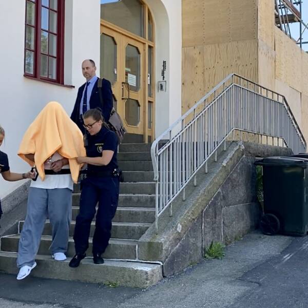En man förs ut från en byggnad med filt över huvudet av två vakter.