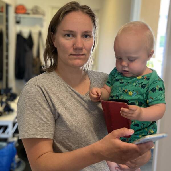 Amelia Luukkonen står med sin ettårige son Elton på armen och håller också i sin mobiltelefon. Hon kollar in i kameran.