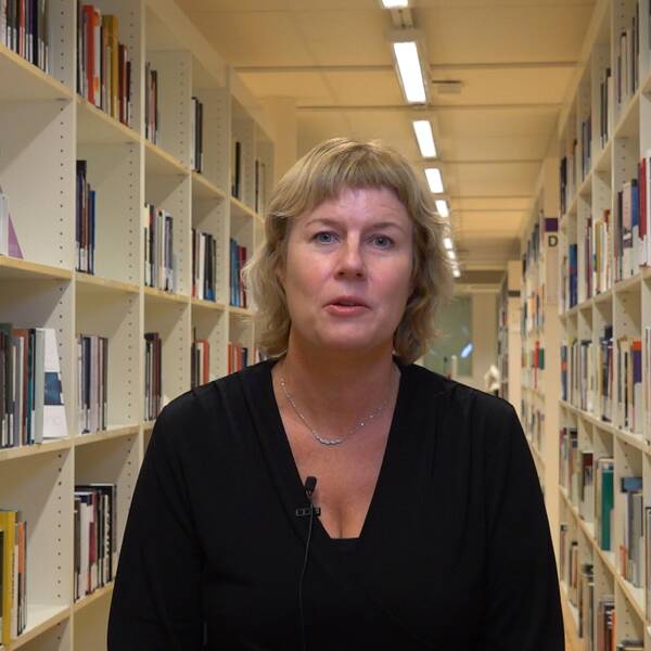 en medelålderskvinna står mellan bokhyllorna i ett bibliotek