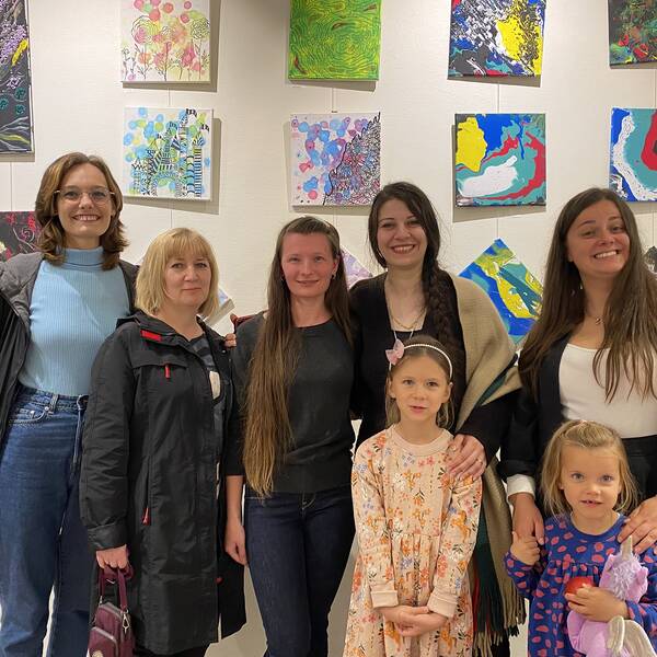 Kvinnor och barn som står framför tavlorna de målat under tre månader under överinseende av en konstnär som står i mitten