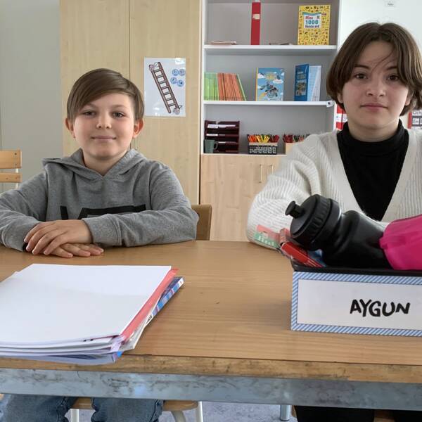 två pojkar i sin skolbänk, med namnskyltar på, ler mot kameran.