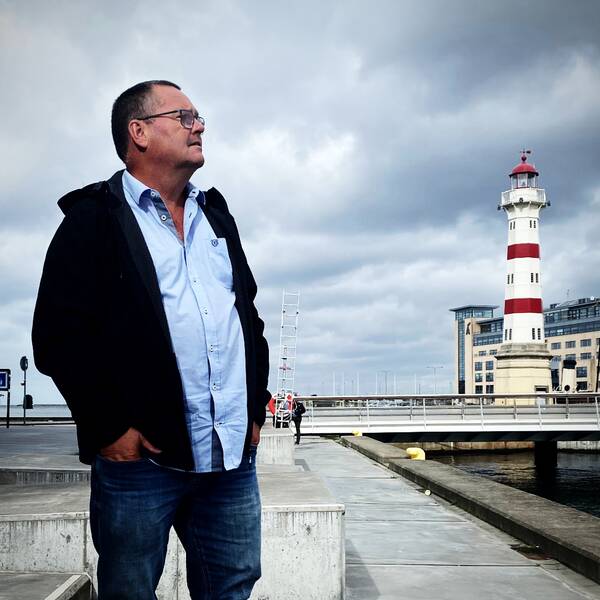 En bild på en man i skjorta och svart jacka som tittar ut över en hamn i Malmö, där intervjun sker.