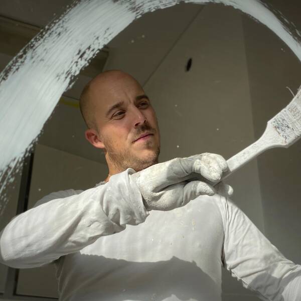 en man ses genom en glasruta, målar en båge med pensel på glaset