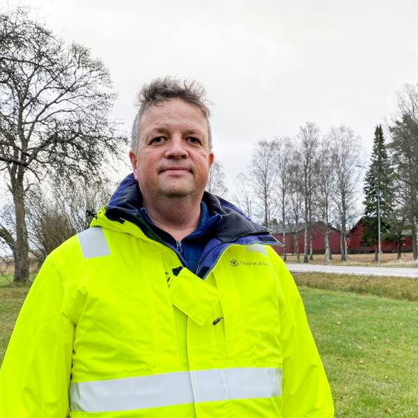 En man med reflexjacka står på gräset bredvid en väg.